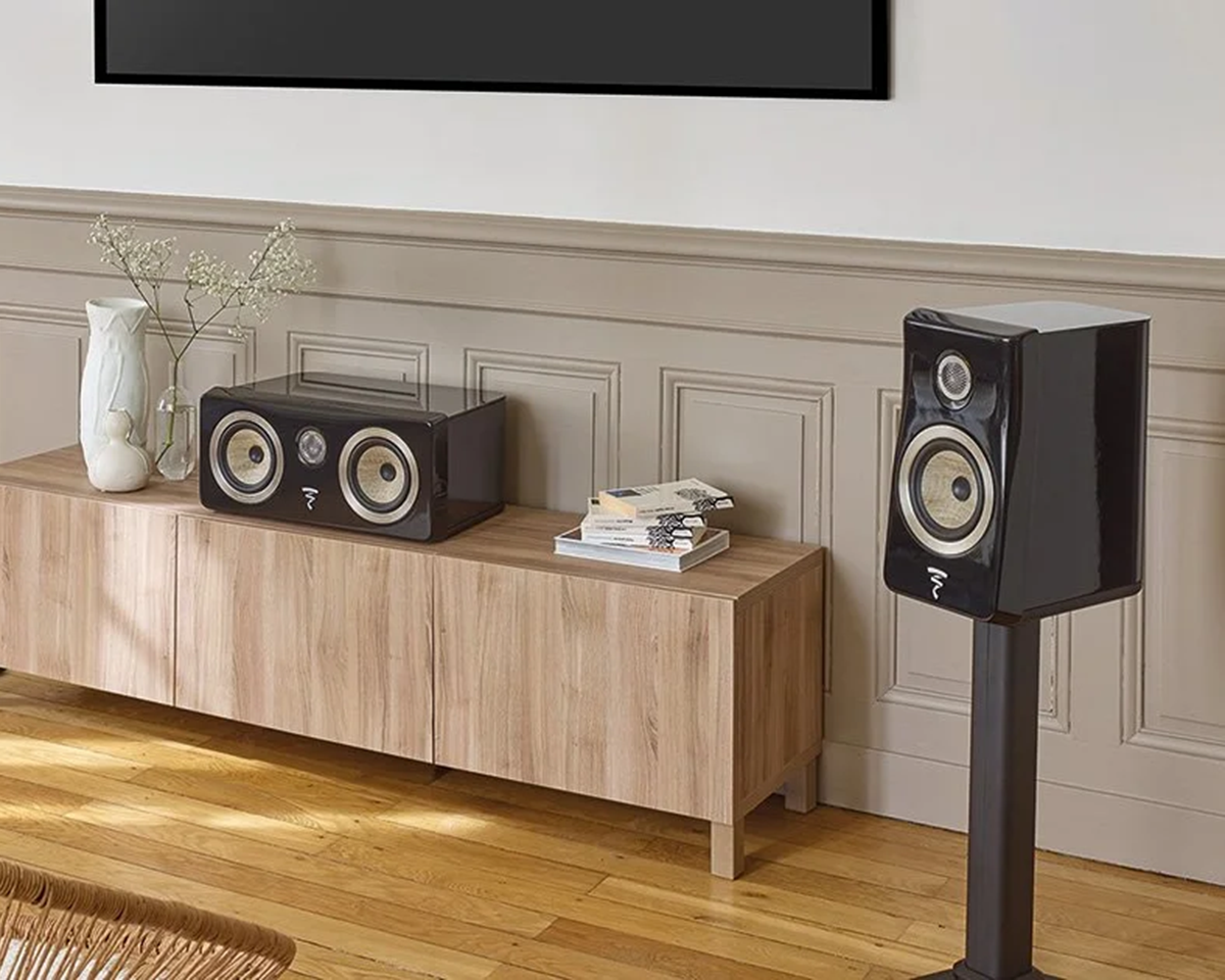 Modern living room with a sleek, black speaker on a stand and a matching speaker on a wooden cabinet. Decor items and books add a cozy touch.