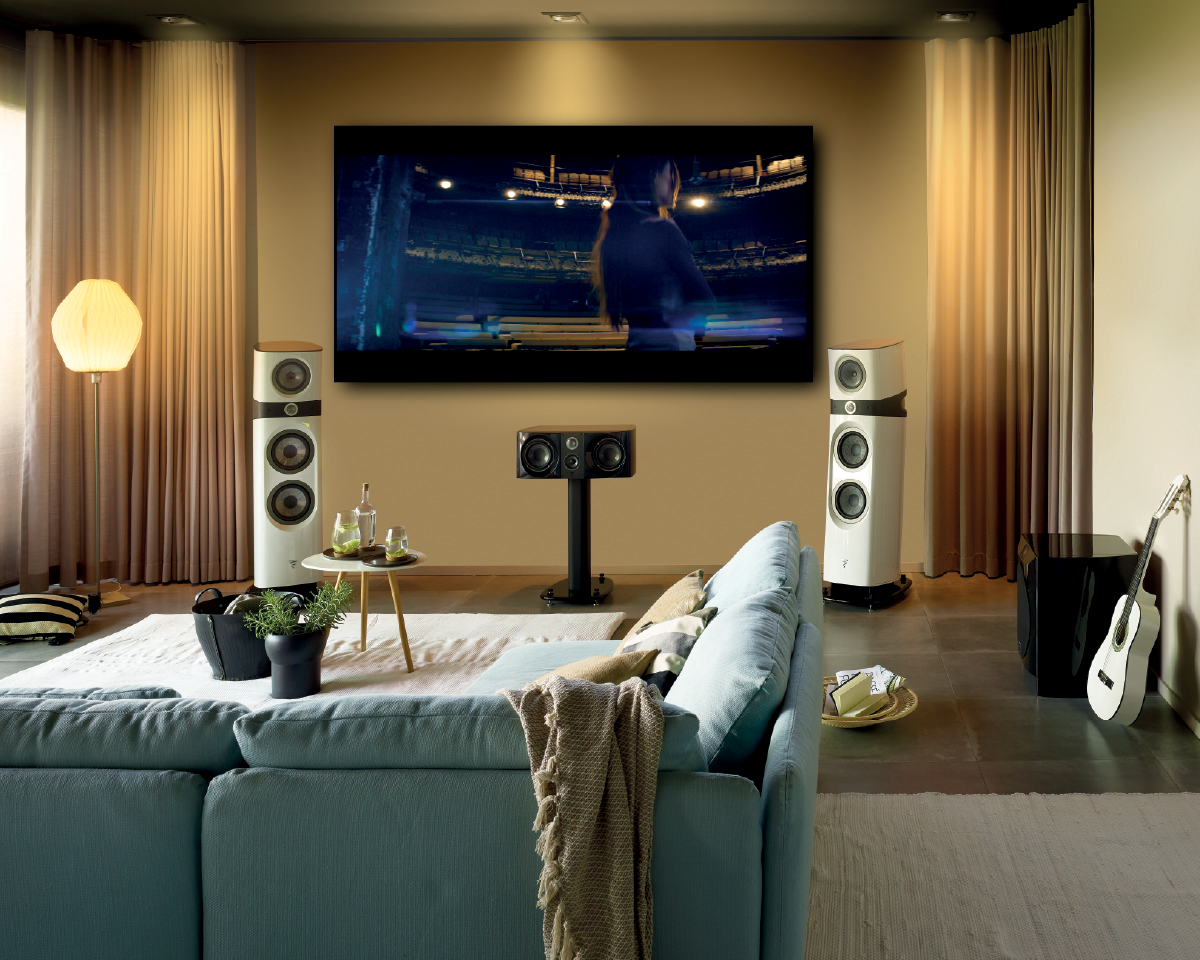 Modern living room with a large flat-screen TV showing a scene, surrounded by high-end speakers. A cozy sofa, guitar, and warm lighting add to the comfort.