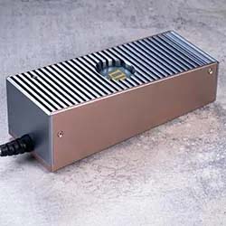 A sleek, rectangular metal device with vertical slats and a visible fan sits on a textured gray surface. It has a cable connected to one end.