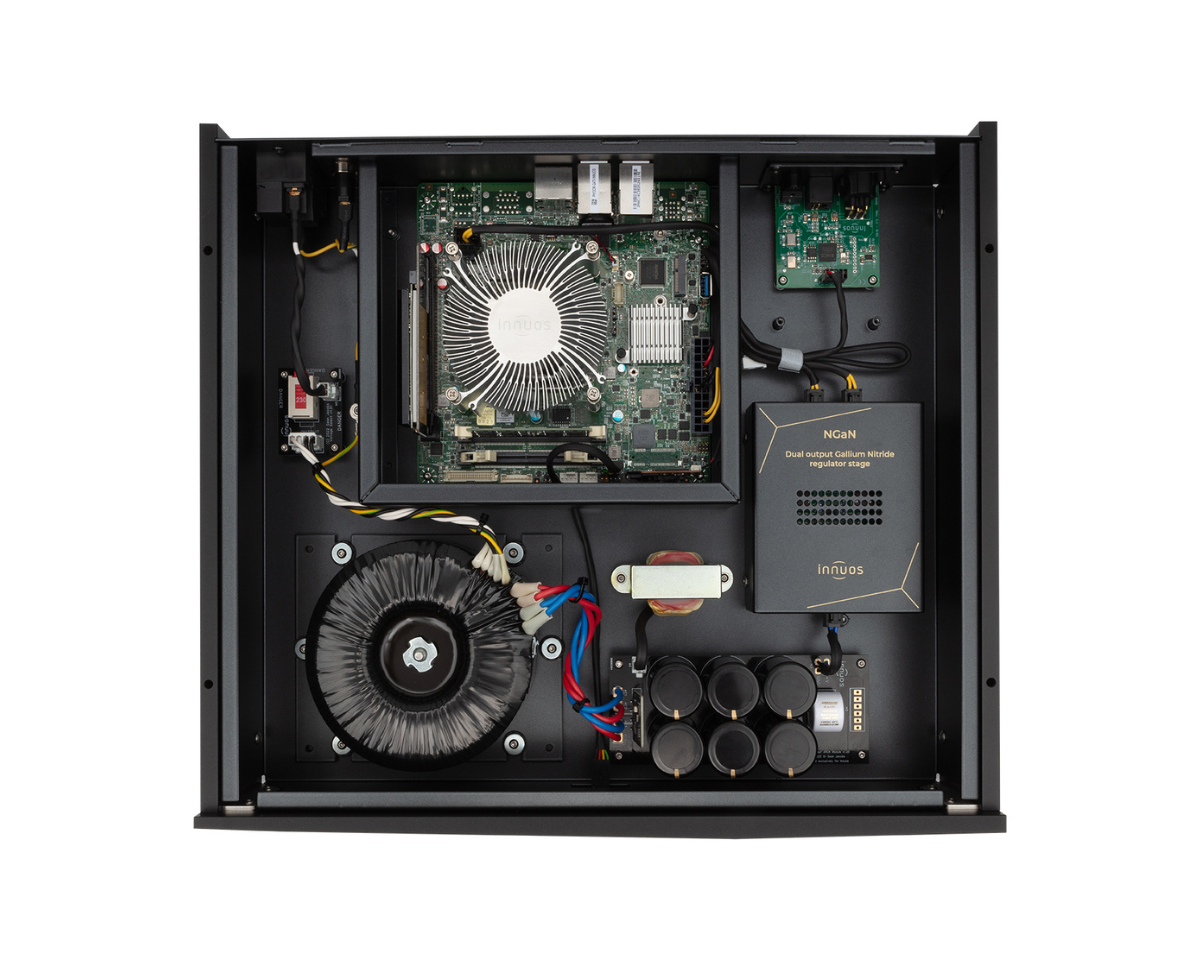 Interior view of a black metal electronic device with a central circuit board and large cooling fan. Visible components include wiring, a transformer, and capacitors, indicating a high-tech, industrial feel.