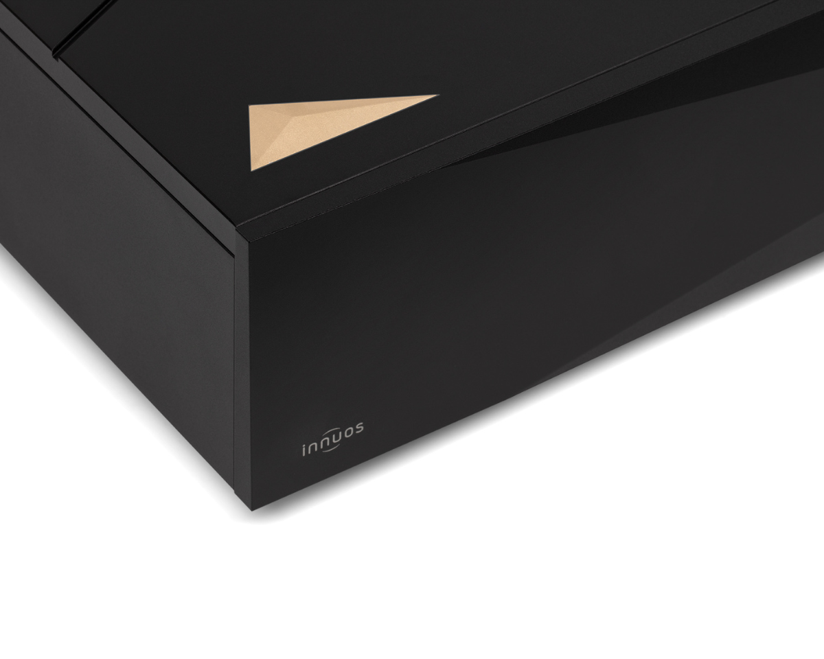 Close-up of a sleek black electronic device with a gold triangular design on top and "innuos" branding on the side, conveying a modern aesthetic.