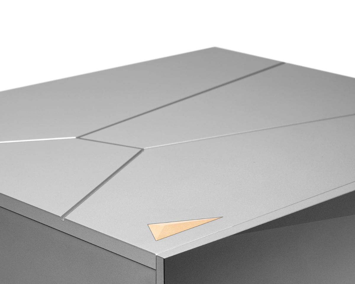 A sleek, silver, geometric object with angular lines and a small, gold triangle accent on the surface, conveying a modern and minimalist design.