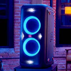 A large speaker with blue LED lights in two circular patterns. It's set against an urban brick wall backdrop, creating a lively, energetic ambiance.