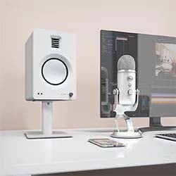 Modern white desk setup with a large computer monitor, white studio speaker, USB microphone, and smartphone, conveying a minimalist, tech-savvy vibe.