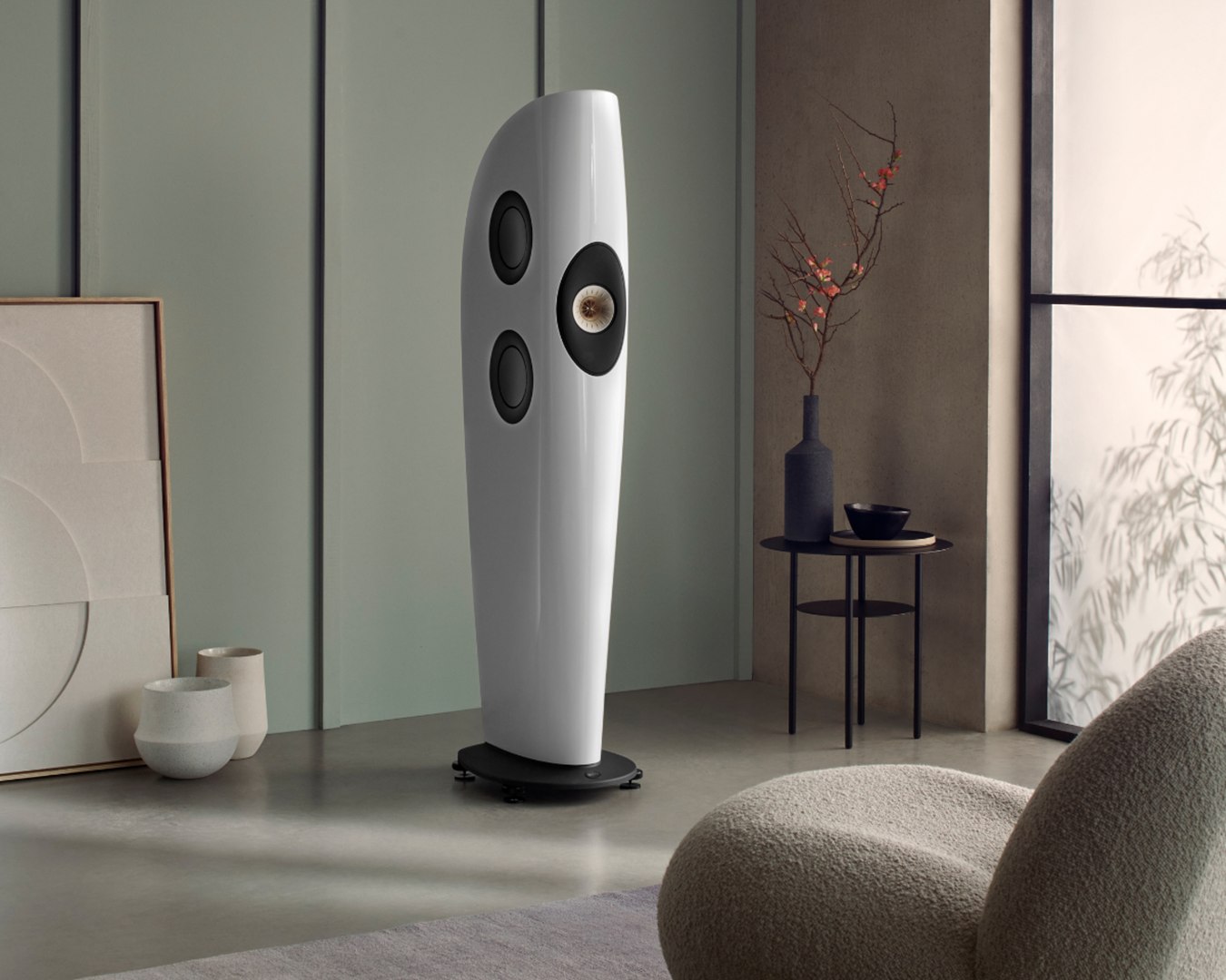 Modern living room featuring a sleek, curved white speaker with three black speakers on a pedestal. Minimalist decor includes abstract art, a side table with a vase, and soft lighting, creating a serene atmosphere.