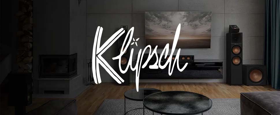 Sophisticated living room with large TV, surround sound system, and wooden floors. Cozy atmosphere with modern furniture. "Klipsch" logo in foreground.