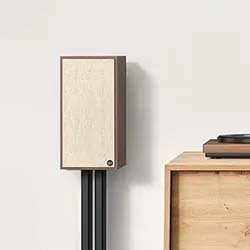 A minimalist room features a wooden speaker with a beige front on a black stand and a wooden cabinet with a turntable, conveying retro elegance.