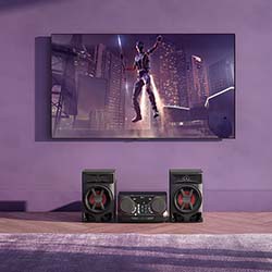 A sleek, modern home theater setup with a large wall-mounted TV displaying an action scene, and powerful speakers below on a purple wall, creating an immersive atmosphere.