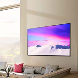 A modern living room with a wall-mounted TV displaying a vibrant pink and purple mountain landscape. Below, a stylish beige couch with colorful cushions.