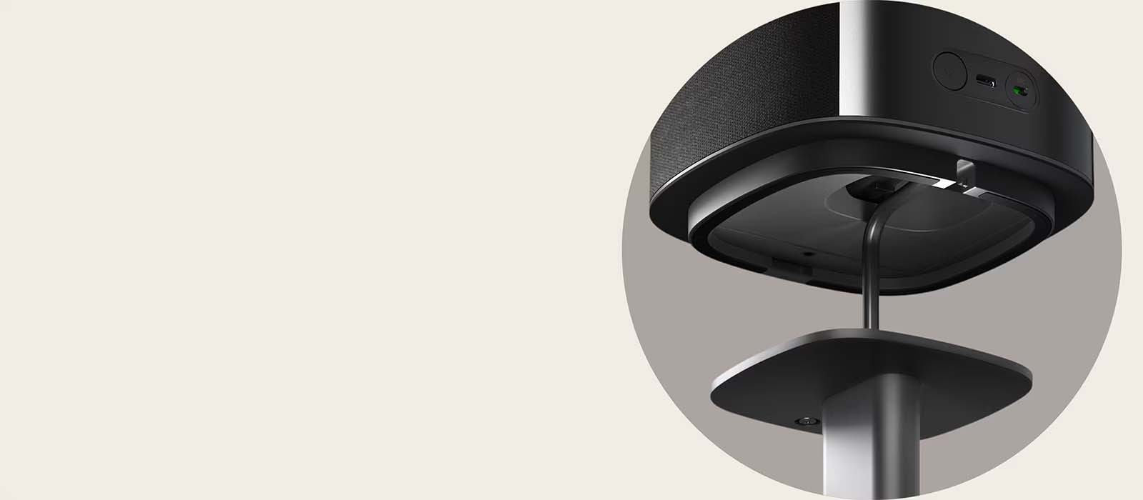 Close-up of a modern speaker mounted on a sleek stand with a visible cable. The light beige background creates a minimalist and contemporary feel.