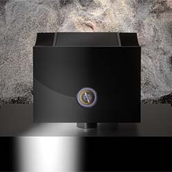 A sleek, black, cube-shaped device with a circular dial on its front sits on a reflective surface against a textured stone background, exuding a modern and sophisticated vibe.