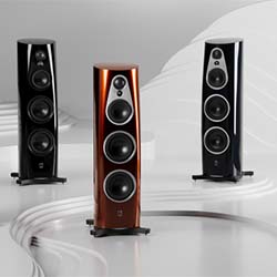 Three sleek, modern floor-standing speakers in black and copper finish are displayed on a smooth, wave-like white surface, evoking elegance and high-tech sophistication.