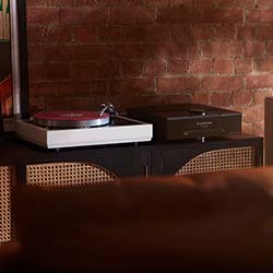 A stylish, modern turntable and speaker on a wooden cabinet against a textured brick wall, evoking a warm, vintage vibe.