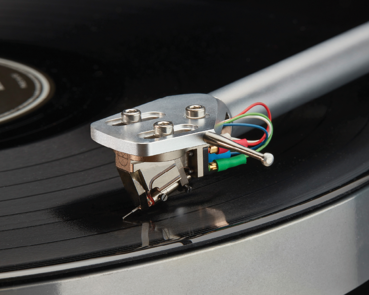 Close-up of a turntable needle on a black vinyl record. The metal tonearm and vibrant colored wires convey a vintage, high-fidelity music experience.