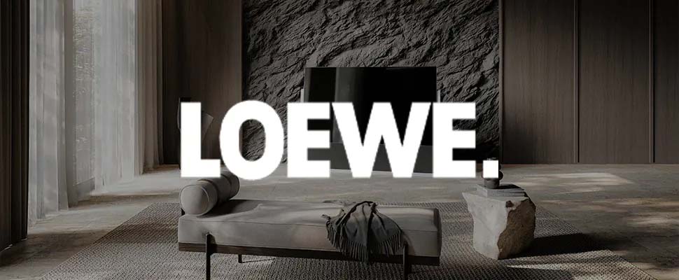 Modern living room with a textured dark wall, minimalist gray chaise lounge, stone coffee table, and sheer curtains. "LOEWE." text overlays the scene.