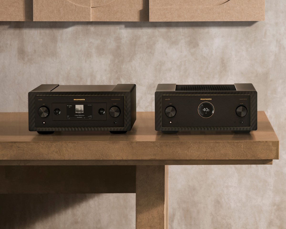 Two sleek black stereo components with knobs and displays sit on a wooden table against a textured gray wall, exuding modern elegance.