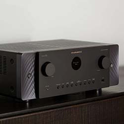 A sleek black audio receiver with two large knobs and multiple buttons sits on a dark wooden surface. The design is modern and minimalist.