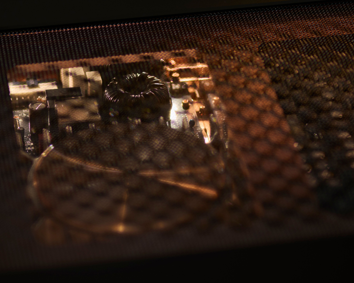 Close-up of computer components seen through a mesh, with dim lighting casting a warm glow, creating a mysterious, tech-focused atmosphere.