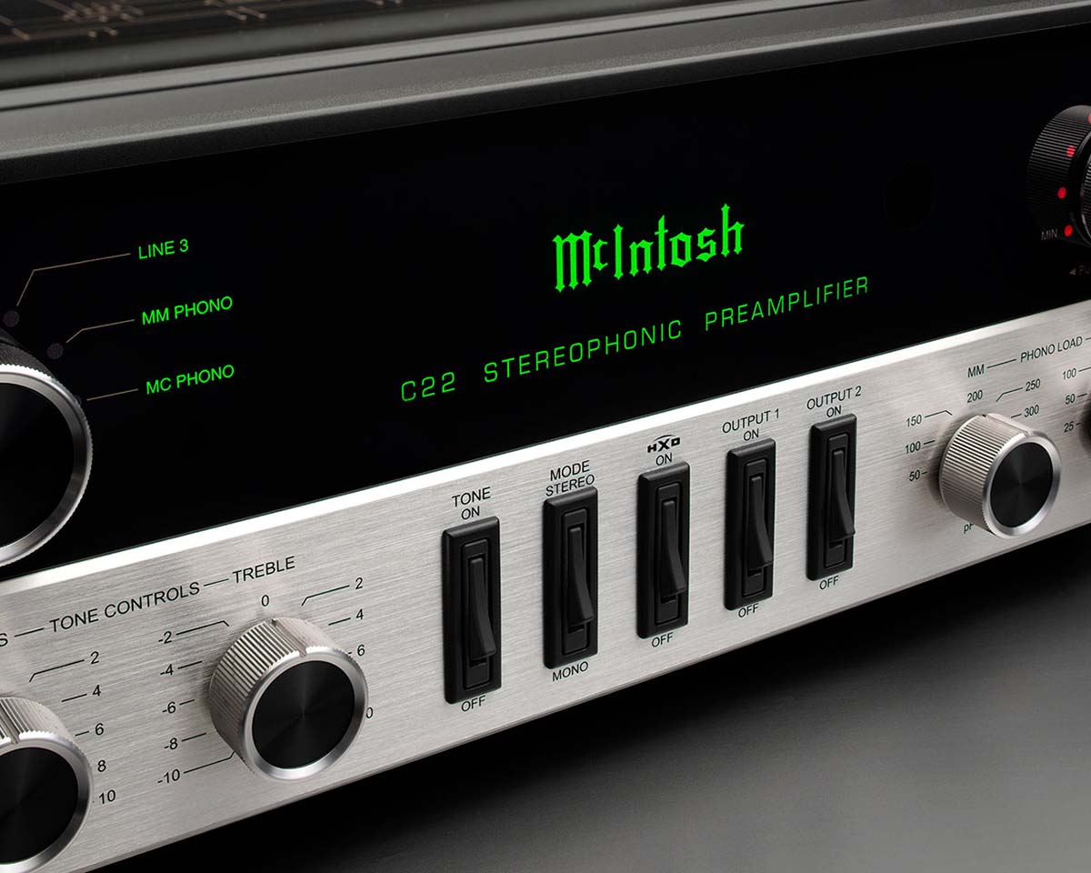 Close-up of a McIntosh C22 stereophonic preamplifier. Features include silver knobs, black switches, and a green-lit display. Sleek, vintage design.