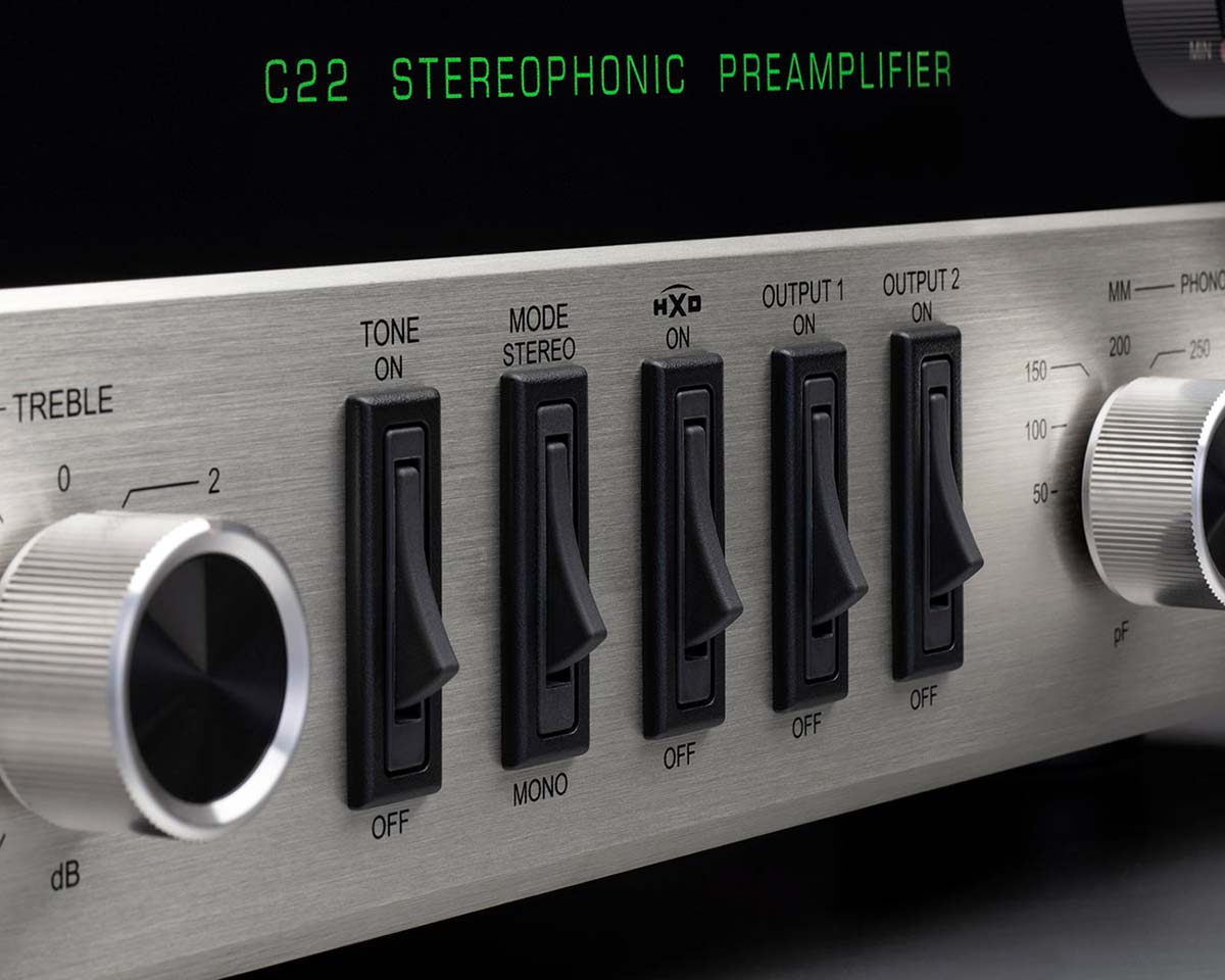 Close-up of a vintage-style C22 Stereophonic Preamplifier panel with switches, knobs, and green LED display. It conveys a sleek, technical aesthetic.