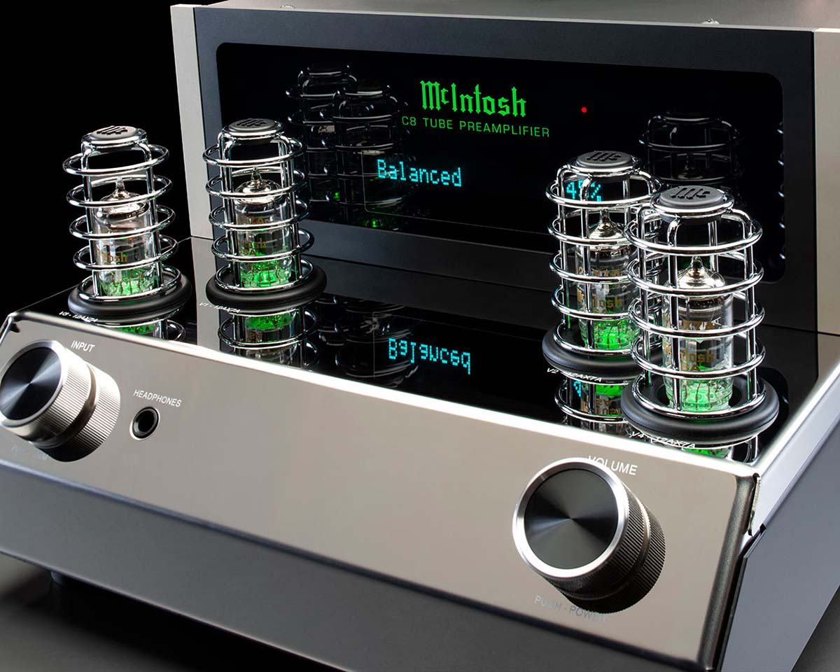 Close-up of a McIntosh C8 tube preamplifier. It features glowing vacuum tubes protected by metallic cages, sleek knobs, and a digital display.
