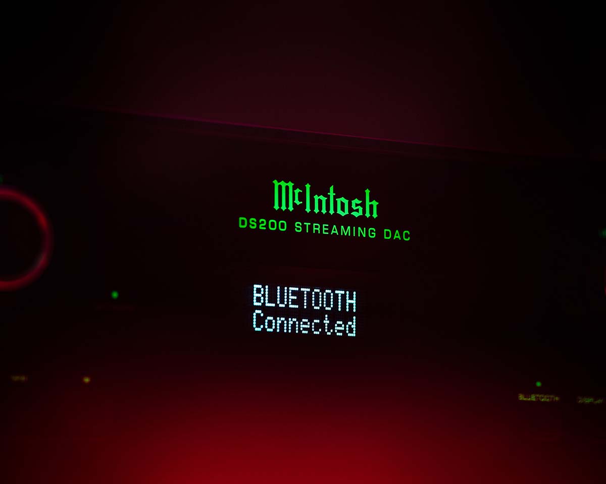 Display screen showing "McIntosh DS200 Streaming DAC" in green neon and "Bluetooth Connected" in white against a dark red background, conveying modern technology.