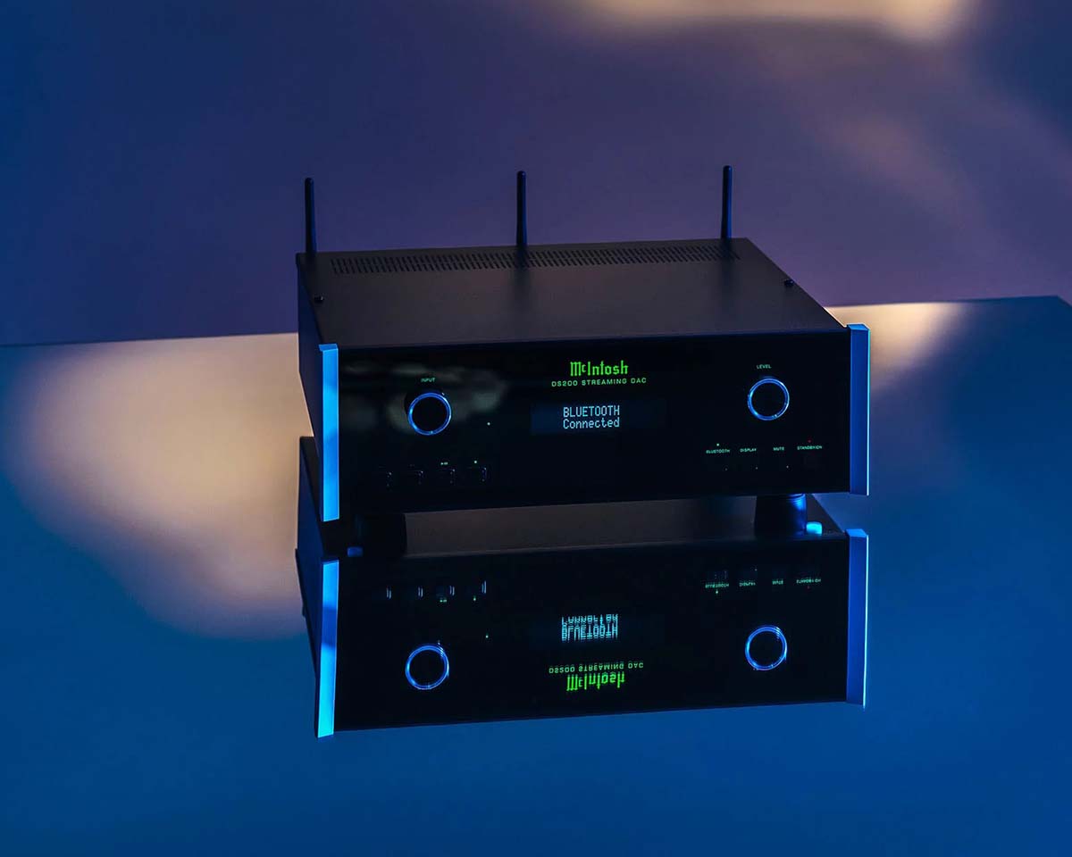 Black audio equipment with two knobs, a digital display reading "BLUETOOTH Connected," reflecting on a glossy blue surface in soft, moody lighting.