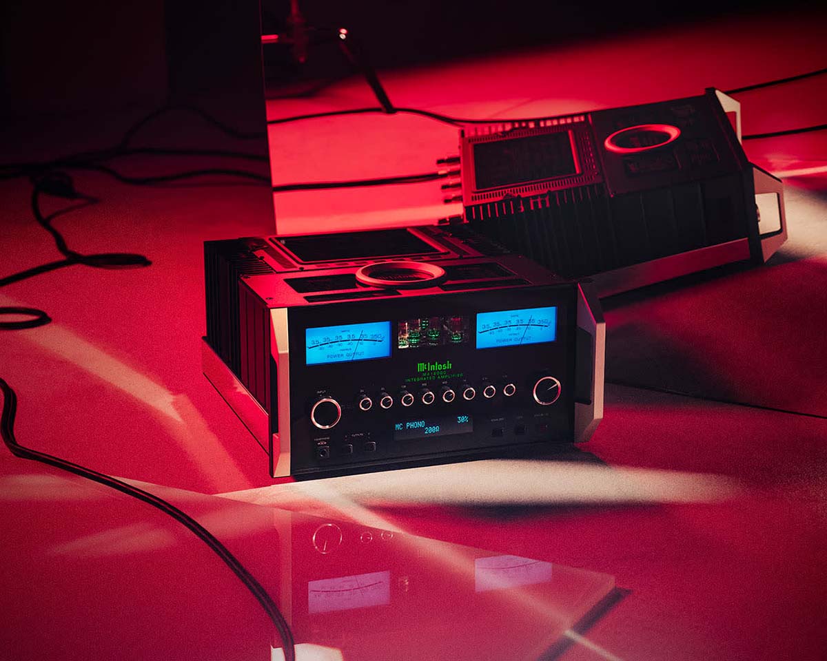 Power amplifiers with glowing blue displays and sleek black design on a red-lit floor, exuding a modern and high-end audio equipment feel.