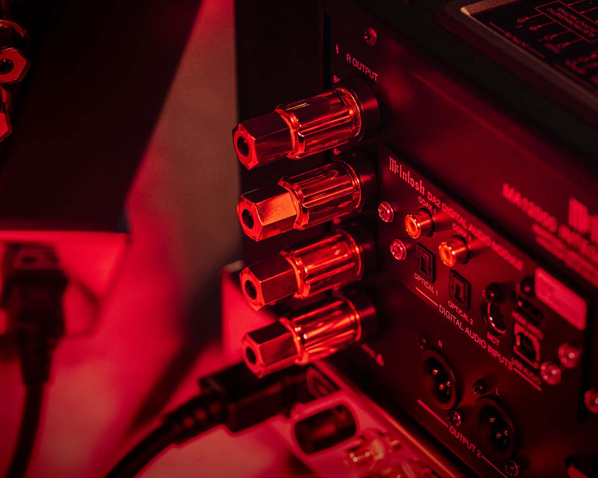 Close-up of a stereo amplifier's rear panel with audio input and output ports, bathed in red lighting, creating a sleek, high-tech feel.