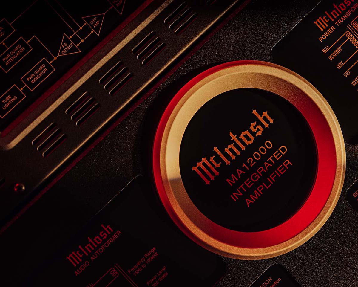 Close-up of a McIntosh MA12000 integrated amplifier, featuring detailed logos and text in red on a black surface. The image has a warm, sophisticated tone.