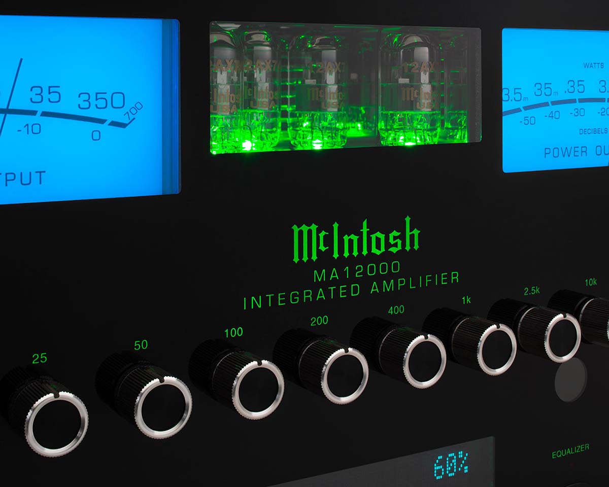 Close-up of a McIntosh MA12000 Integrated Amplifier with glowing green tubes and blue meter displays. Black dials with silver trim denote controls, evoking a sleek, high-tech vibe.