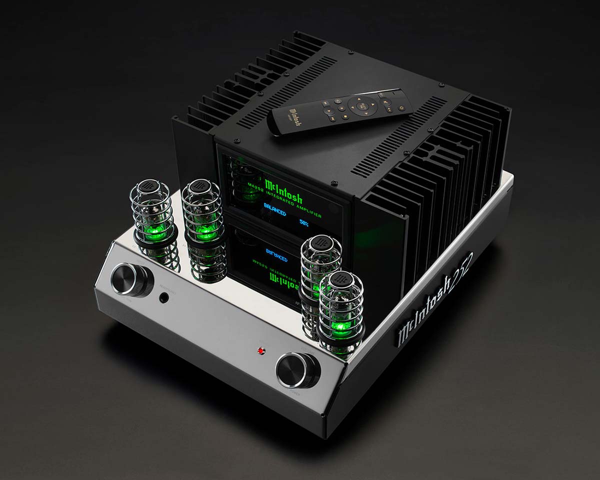 High-end McIntosh audio amplifier with glowing green tube lights and a remote control on top, set against a sleek black background.