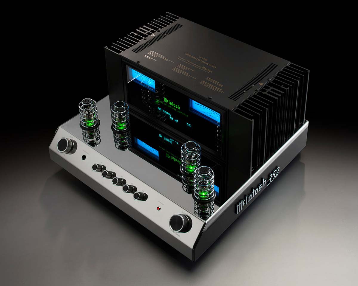 A sleek audio amplifier with a modern silver base, cylindrical glass components with green lights, and black vents. Blue-lit control panels display text.