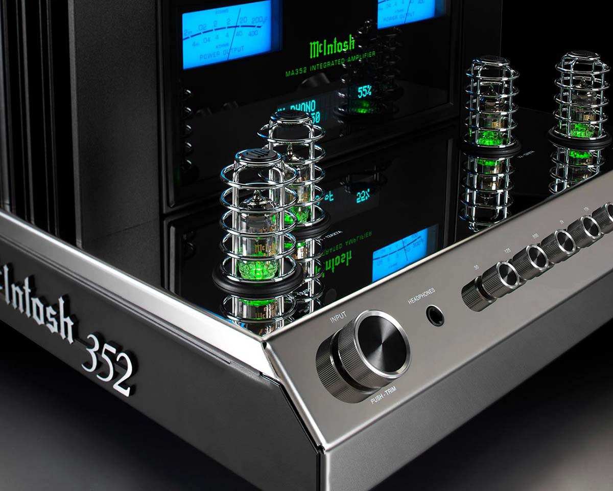 Close-up of a McIntosh 352 amplifier. It features a sleek metallic design, glowing green tubes, and retro dials, exuding a high-tech, vintage vibe.