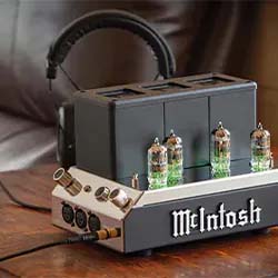 A sleek McIntosh audio amplifier features four glowing vacuum tubes, set on a wooden surface with headphones resting on top, exuding a vintage high-end vibe.