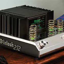 Vintage audio amplifier with silver and black design on a wooden surface, featuring glowing tubes and a sleek, modern aesthetic.