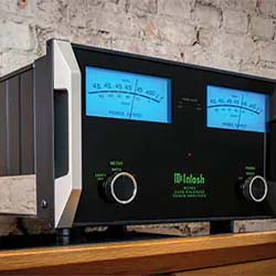 A vintage audio amplifier with a black and silver exterior sits on a wooden shelf. Two glowing blue meters and green text on the front panel offer a classic, retro look.
