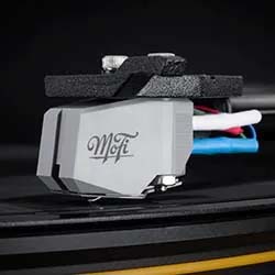 Close-up of a MoFi turntable cartridge on a vinyl record. The tone is modern and sleek, with focus on the stylus and tonearm against a dark background.