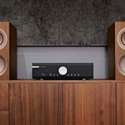 A sleek black audio receiver with a large silver knob is centered on a wooden cabinet, flanked by two tall brown speakers, creating a modern and elegant setup.