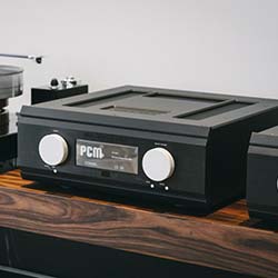 A sleek black audio component with a digital PCM display and two large white knobs, set on a wooden shelf, conveying a modern and high-tech feel.