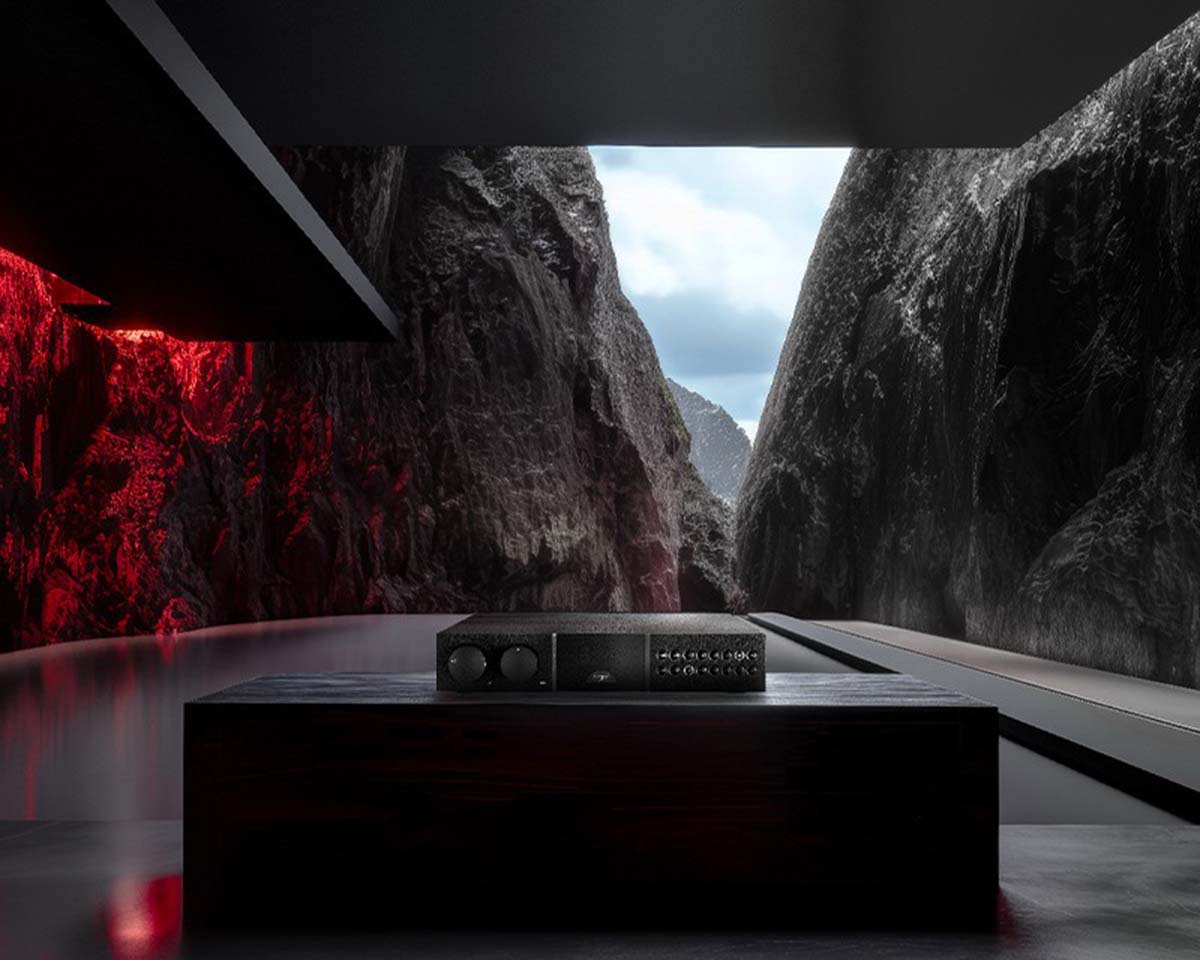 A sleek black audio amplifier sits on a wooden table in a modern room. It overlooks dramatic cliffs and a cloudy sky, creating an intense, futuristic ambiance.