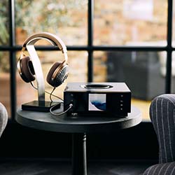 A pair of headphones on a stand beside an audio device on a small round table, set against a bright window, creating a cozy, modern ambiance.