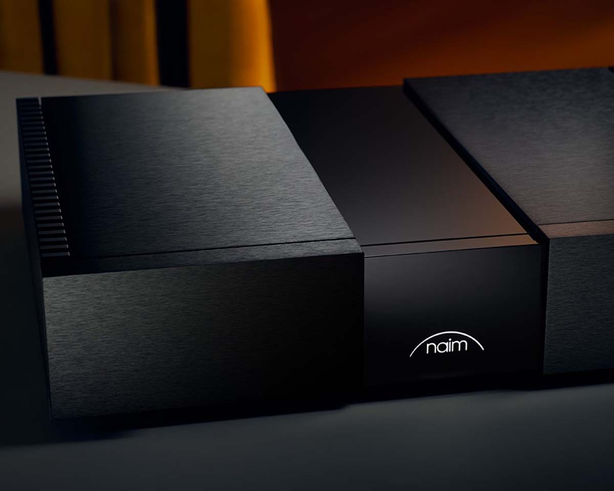 Sleek black audio component with a minimalist design, illuminated "naim" logo, and textured surfaces. The atmosphere is modern and sophisticated.