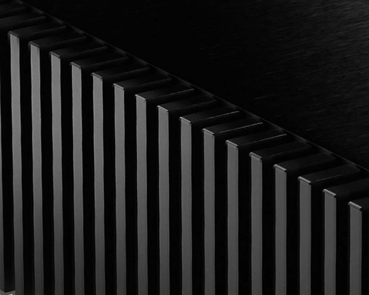 Close-up of a sleek, black, grooved surface with vertical lines casting shadows, creating a minimalist and modern texture. The tone is sleek and industrial.