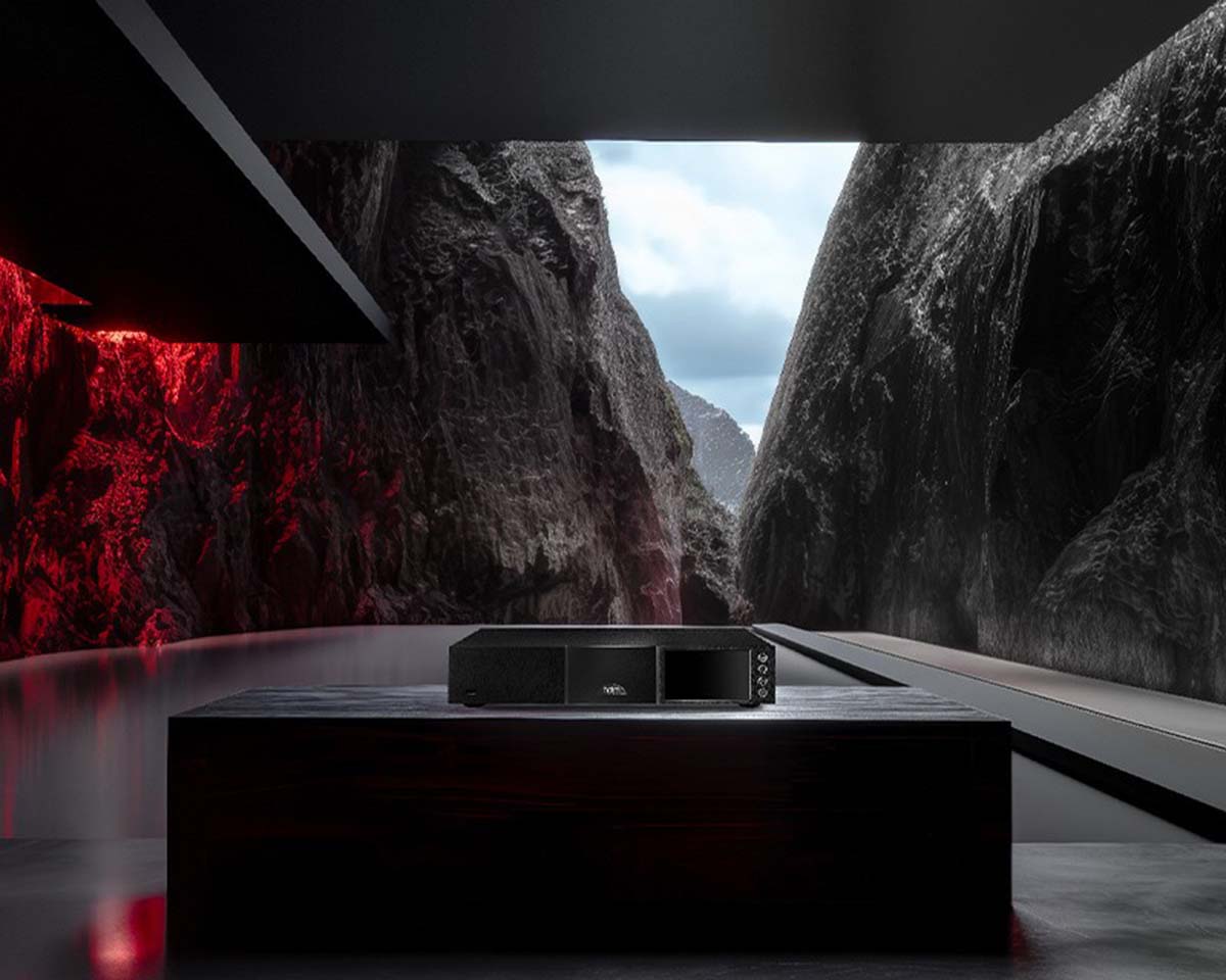 Sleek audio equipment on a dark wood table in a modern room, framed by dramatic red and gray lighting with towering canyon cliffs in the background.