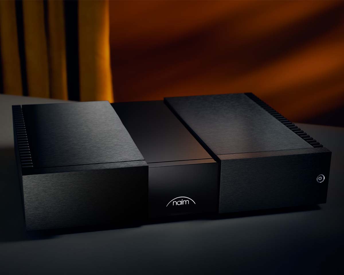 Sleek black audio amplifier with a brushed metal finish, illuminated logo, and power button on the right. Set against an elegant, softly lit background.