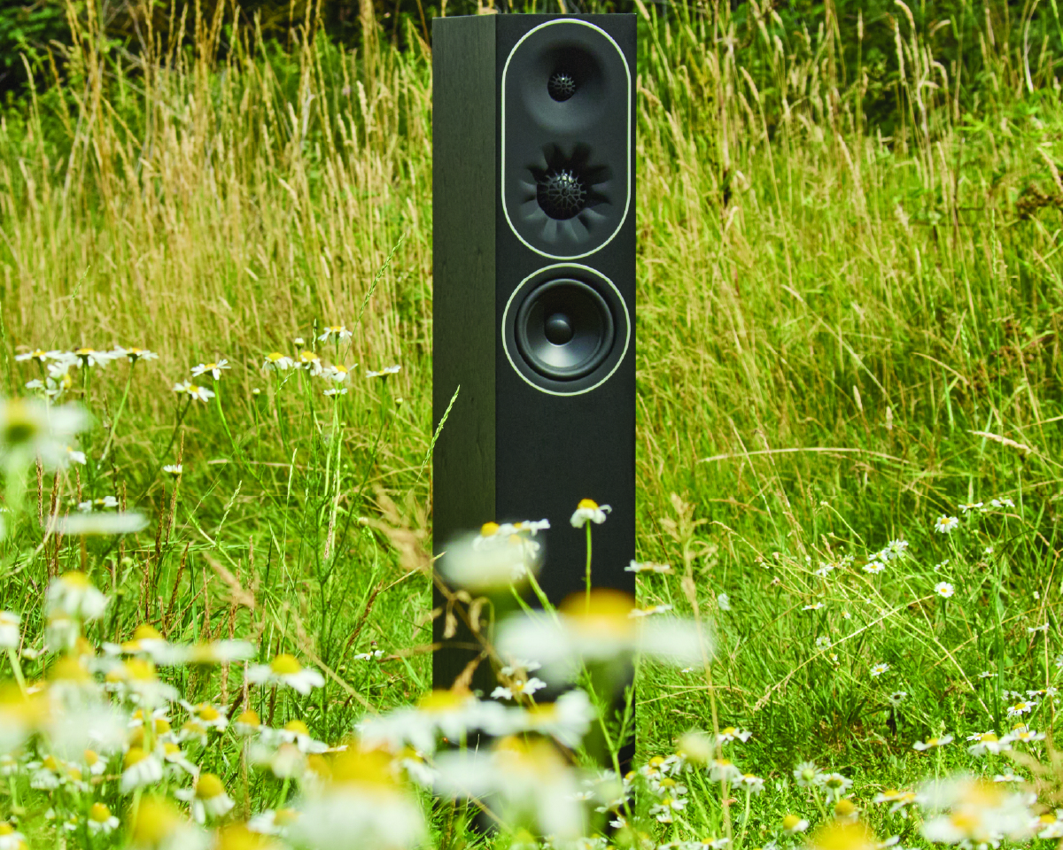 A tall speaker stands amidst a field of wildflowers and tall grass, blending technology with nature. The scene conveys a sense of tranquility and harmony.