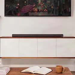 A cozy living room setup features a sleek black soundbar on a minimalist white cabinet, an open book and mug on a wooden table, suggesting a calm ambiance.