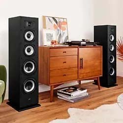 A modern living room with tall black speakers flanking a wooden cabinet. On top, a record player and art piece create a warm, retro vibe.