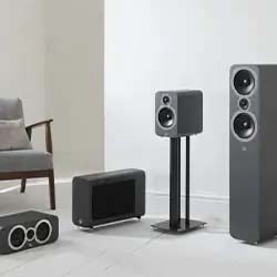 Modern living room with a sleek audio system, including floor-standing, bookshelf, and subwoofer speakers. Minimalist decor with a mid-century chair.